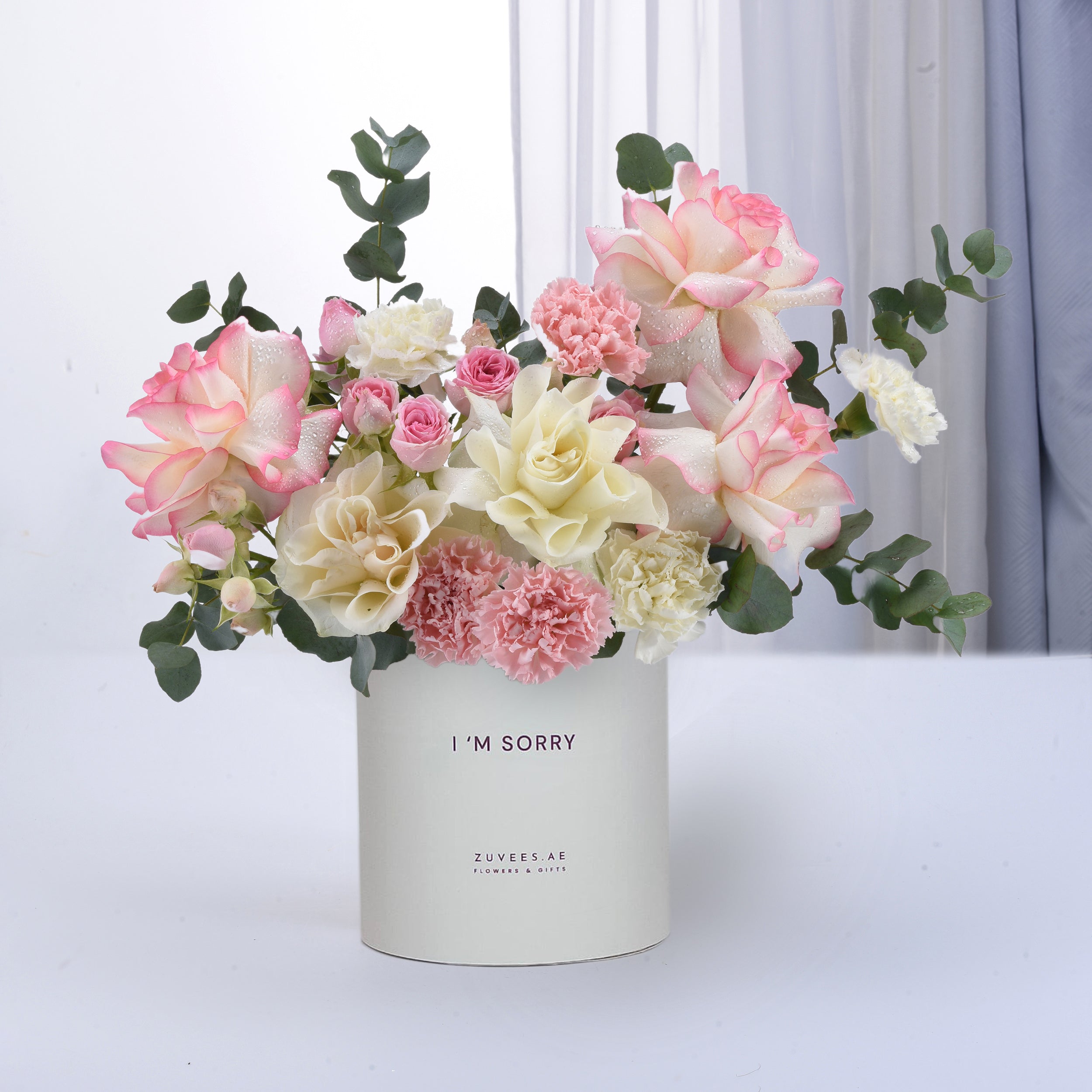 Soft pink and white roses, carnations, and eucalyptus in minimalist white vase with “I&