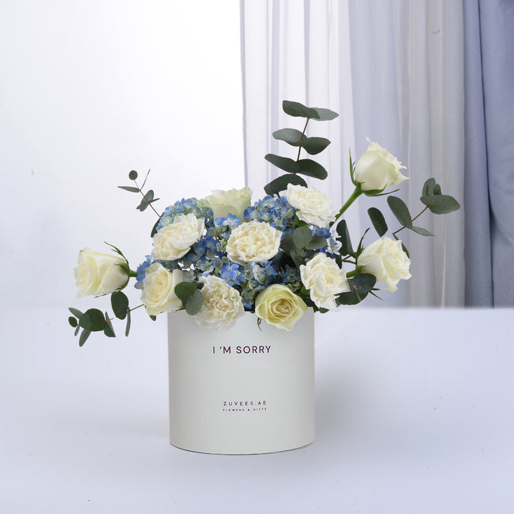 White roses and blue hydrangeas in minimalist white box with "I&