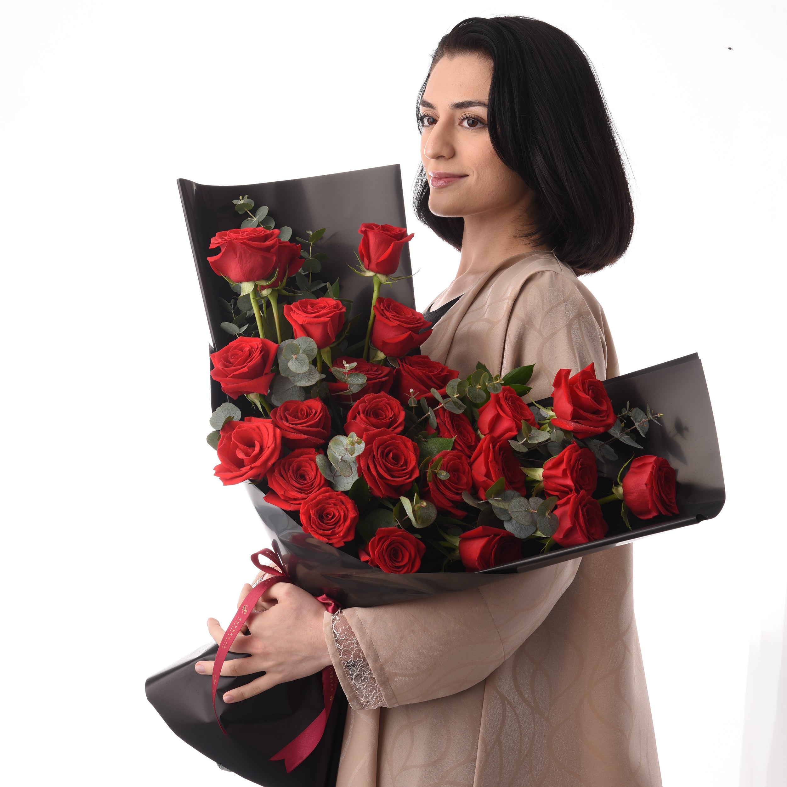 Woman holds lush red rose bouquet wrapped in sleek black paper with burgundy ribbon.