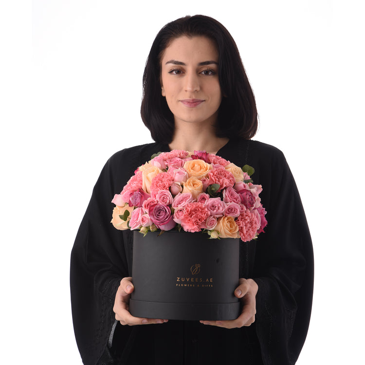 Woman holds black box filled with vibrant pink and peach roses.