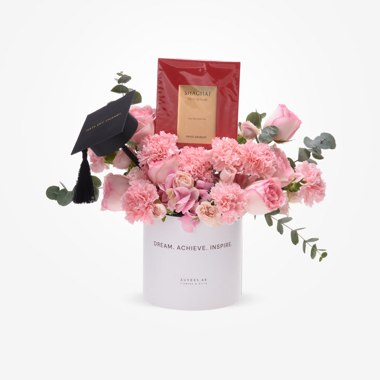 Pink roses and carnations in white vase with graduation cap and Shaghaf perfume.