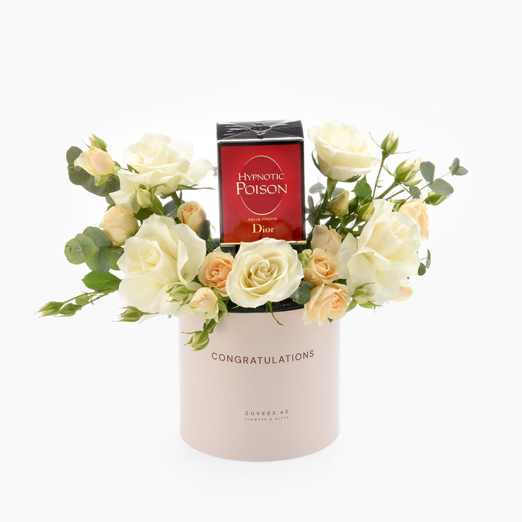 Elegant white roses and eucalyptus surround a Dior Hypnotic Poison bottle in a blush "Congratulations" cylinder.