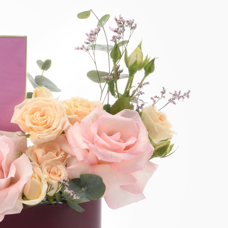 Soft peach and pink roses with lavender sprigs in a deep purple vase.