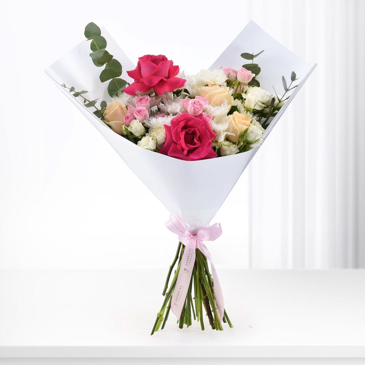 Vibrant pink, peach, and white roses with eucalyptus, elegantly wrapped in white paper with pink ribbon.
