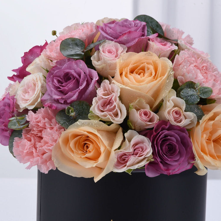Vibrant pink, purple, and peach roses with dewdrops in sleek black box.
