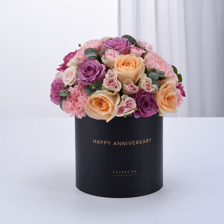 Black box holds vibrant pink, purple, and peach roses with "Happy Anniversary" gold text.