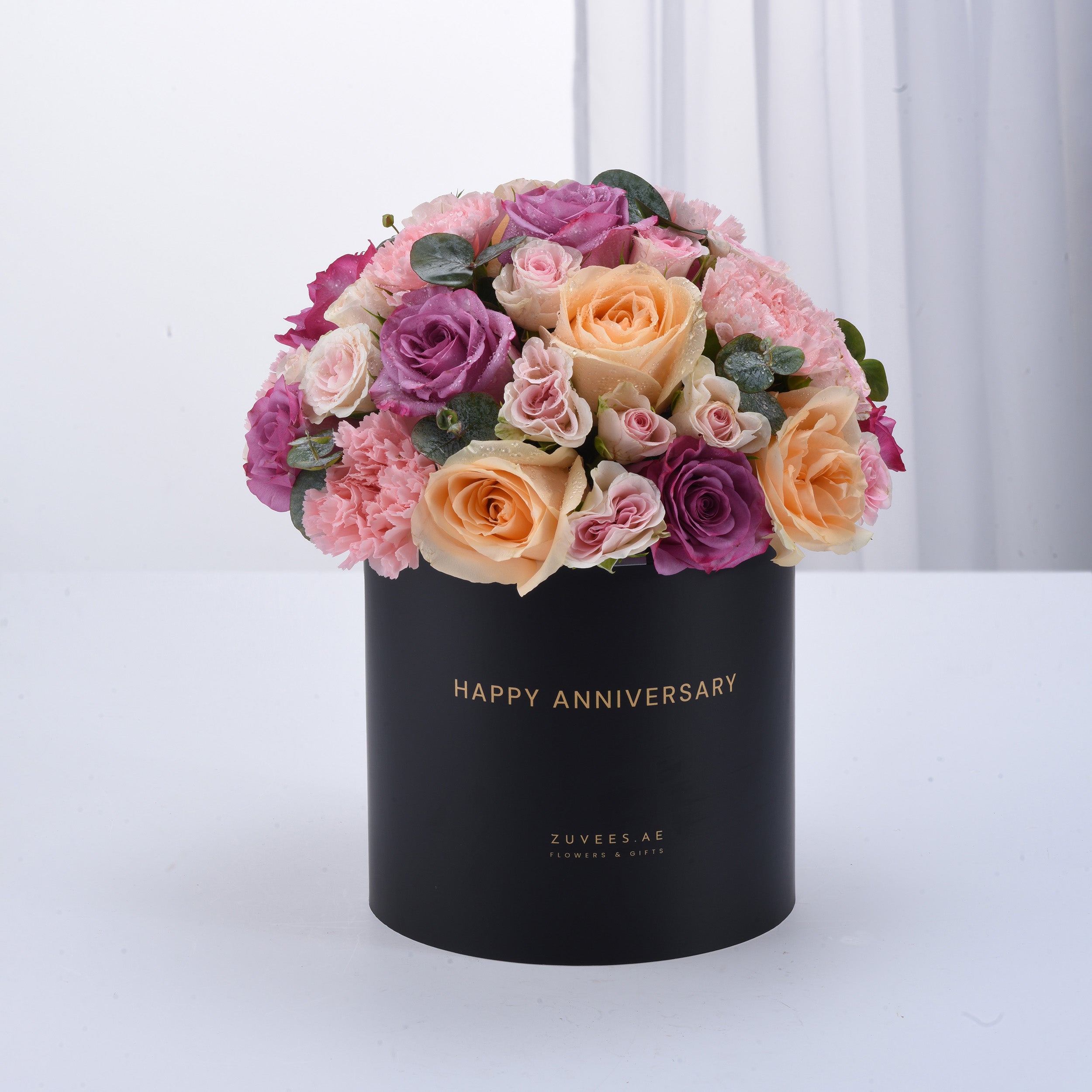 Black box holds vibrant pink, purple, and peach roses with "Happy Anniversary" gold text.