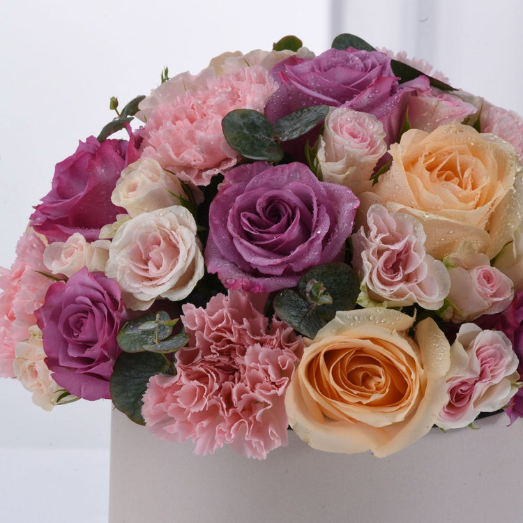 Vibrant bouquet of pink, purple, and peach roses with dewdrops and greenery.