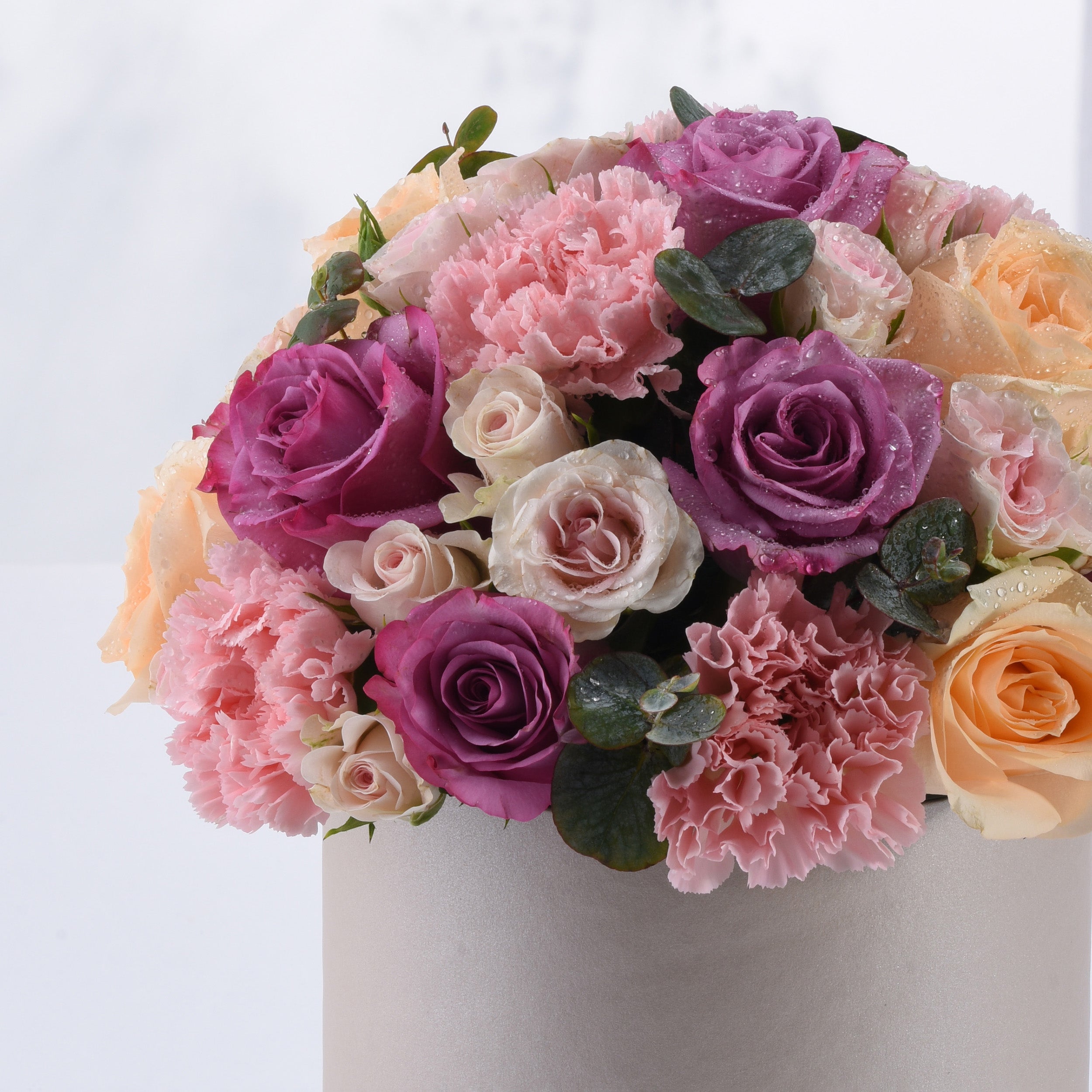 Soft pink, purple, and peach roses with carnations and dewdrops in a silver vase.