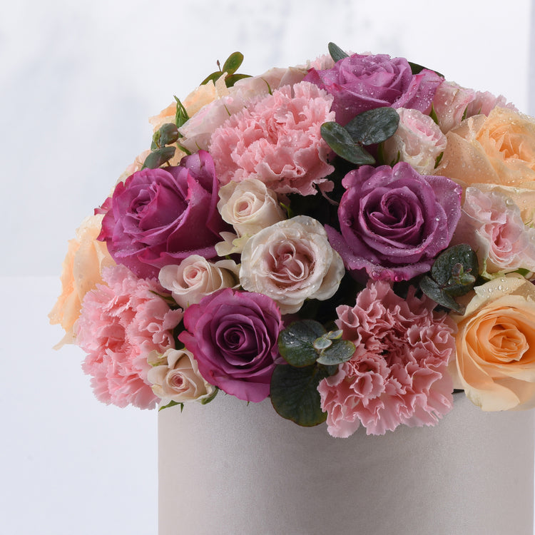 Soft pink, purple, and peach roses with carnations and dewdrops in a silver vase.
