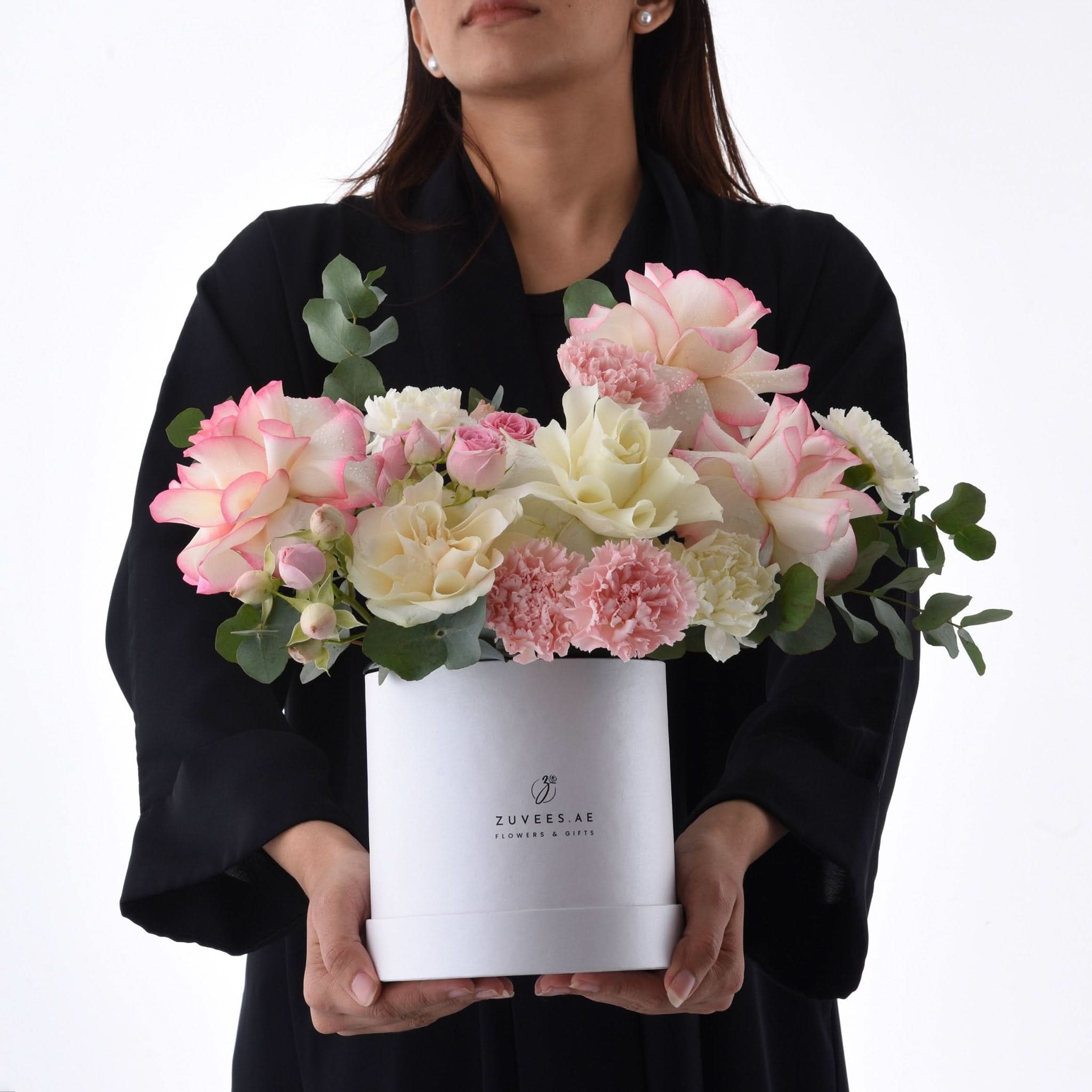 Elegant pink and cream roses with carnations in a white Zuvees gift box, held by woman.