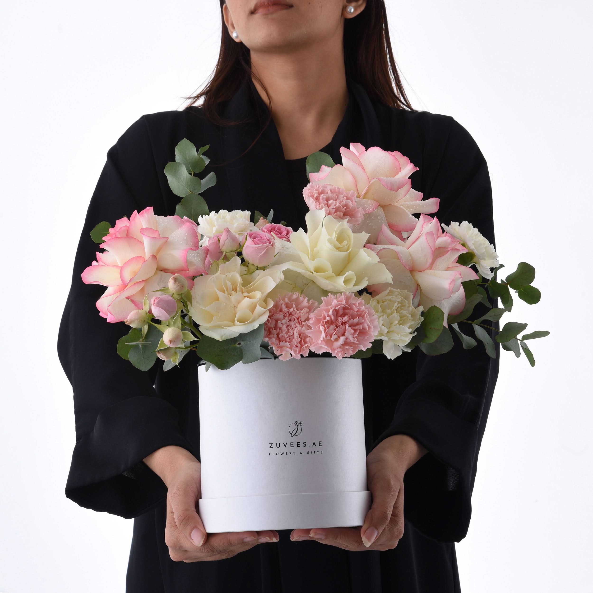 Elegant pink and cream roses with carnations in a white Zuvees gift box, held by woman.
