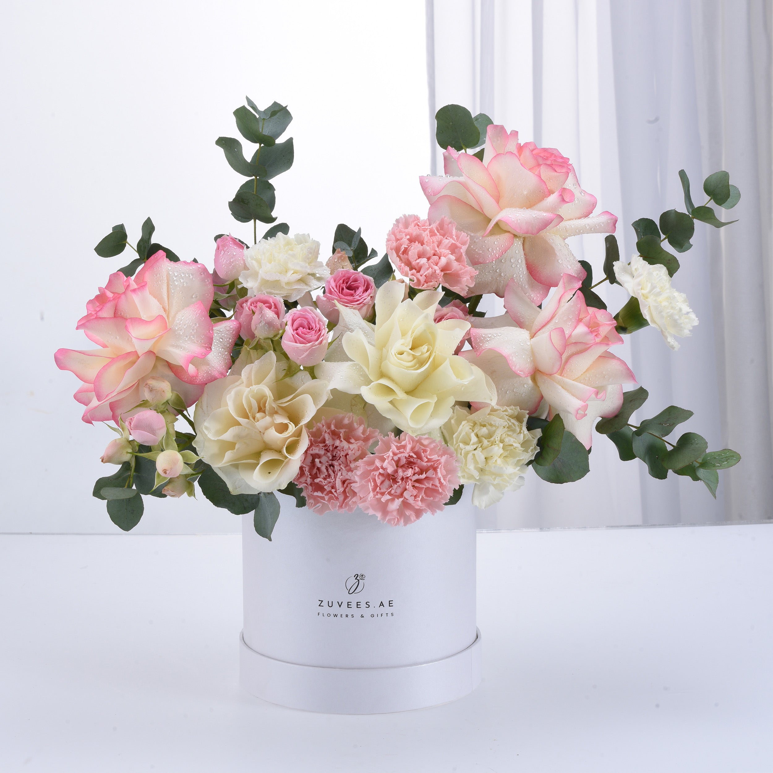 Elegant pastel roses and carnations in white box, dewdrops, eucalyptus.