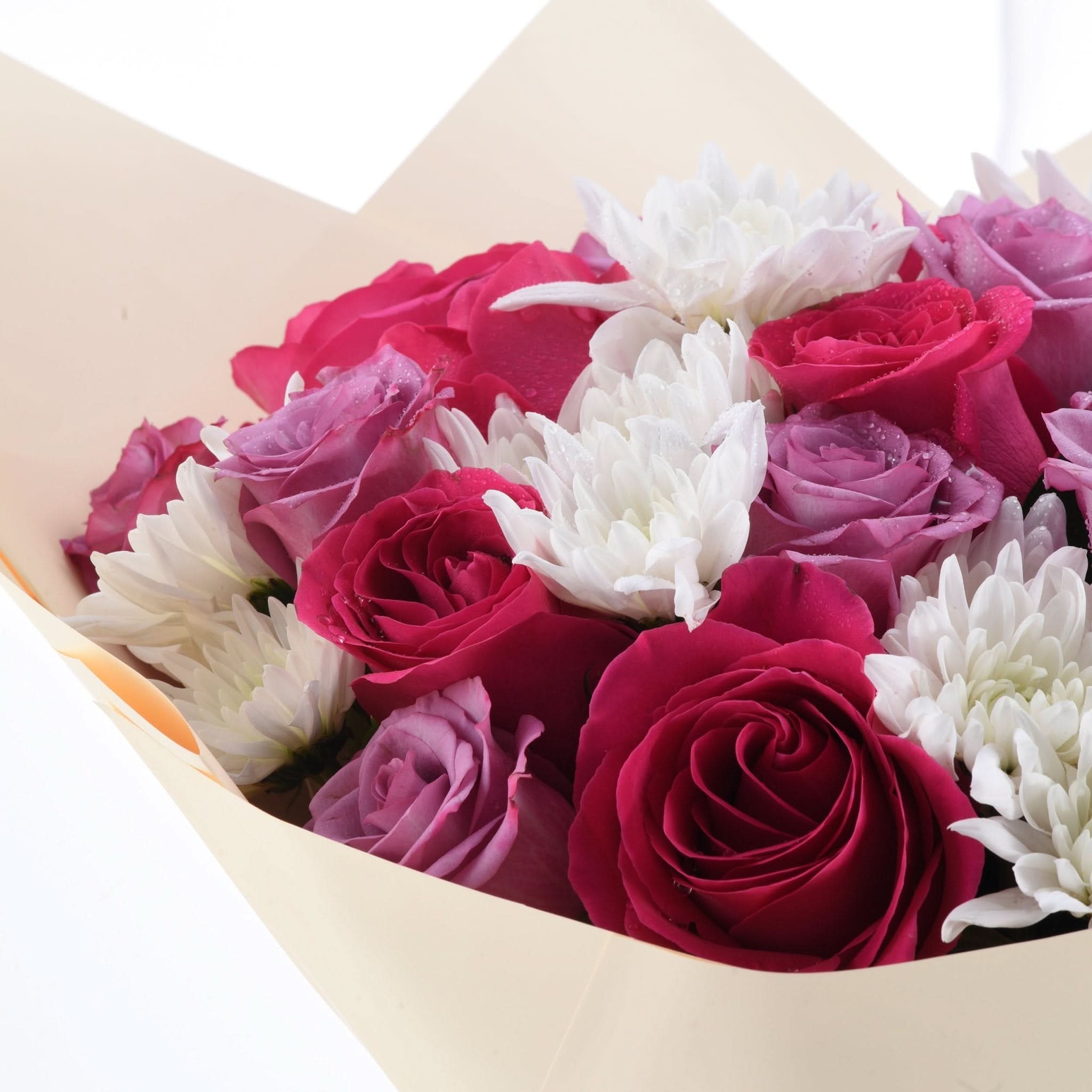 Vibrant red, pink roses and white chrysanthemums nestled in cream paper.