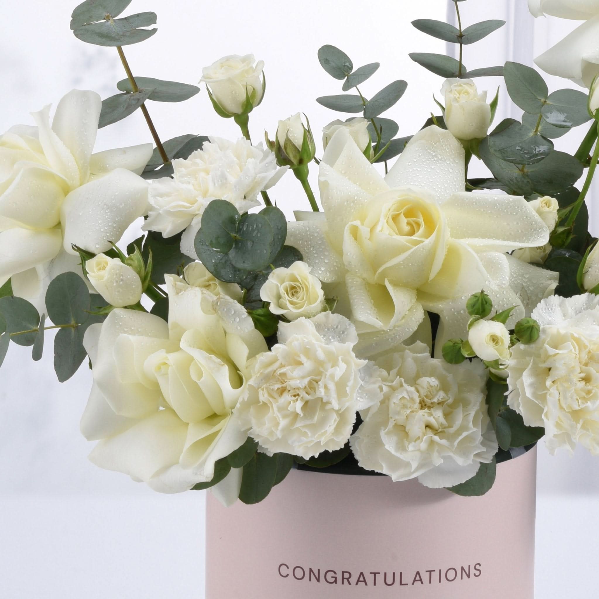 White roses and carnations with dewdrops in a pink "Congratulations" vase.