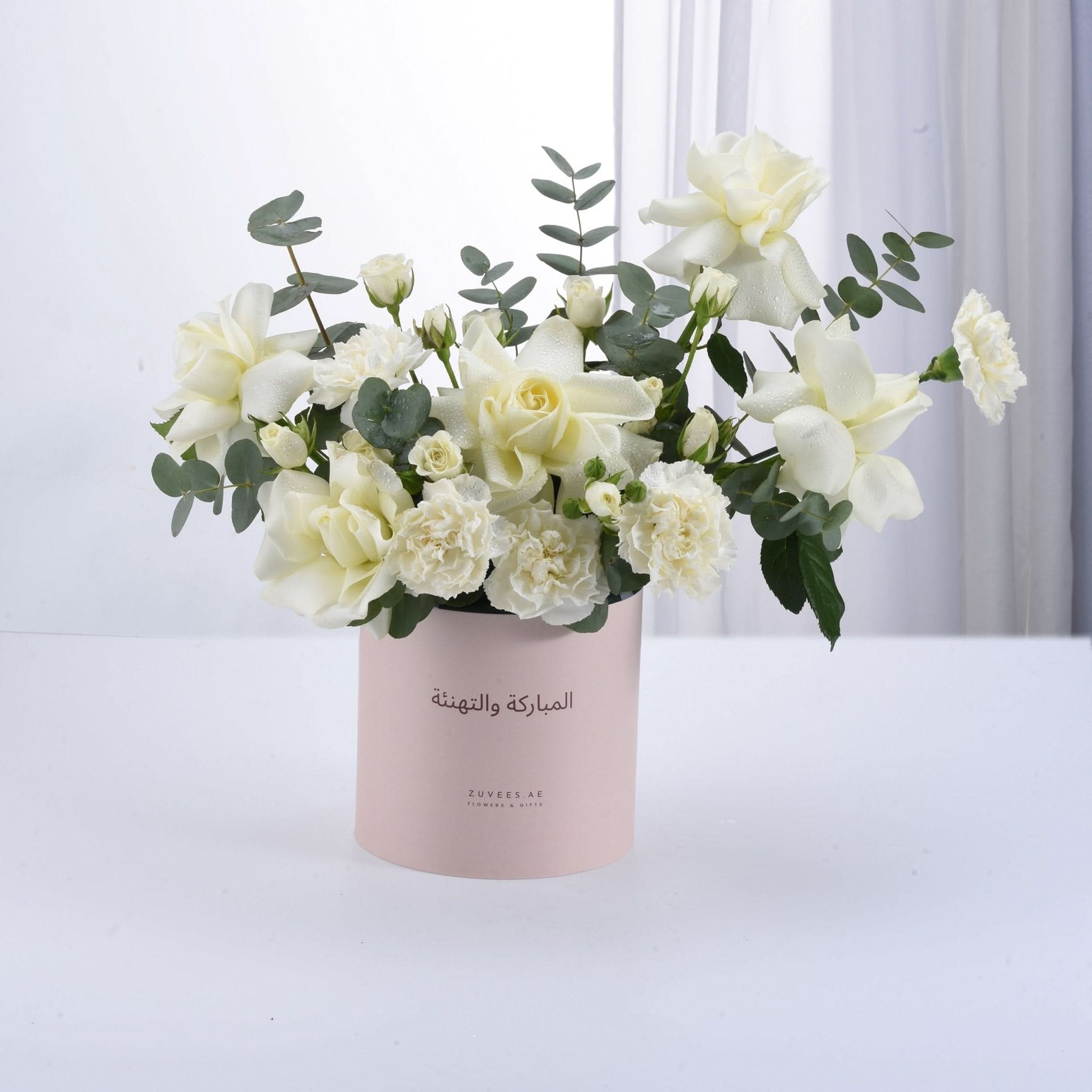 Soft white roses and carnations in pink box with Arabic greeting.
