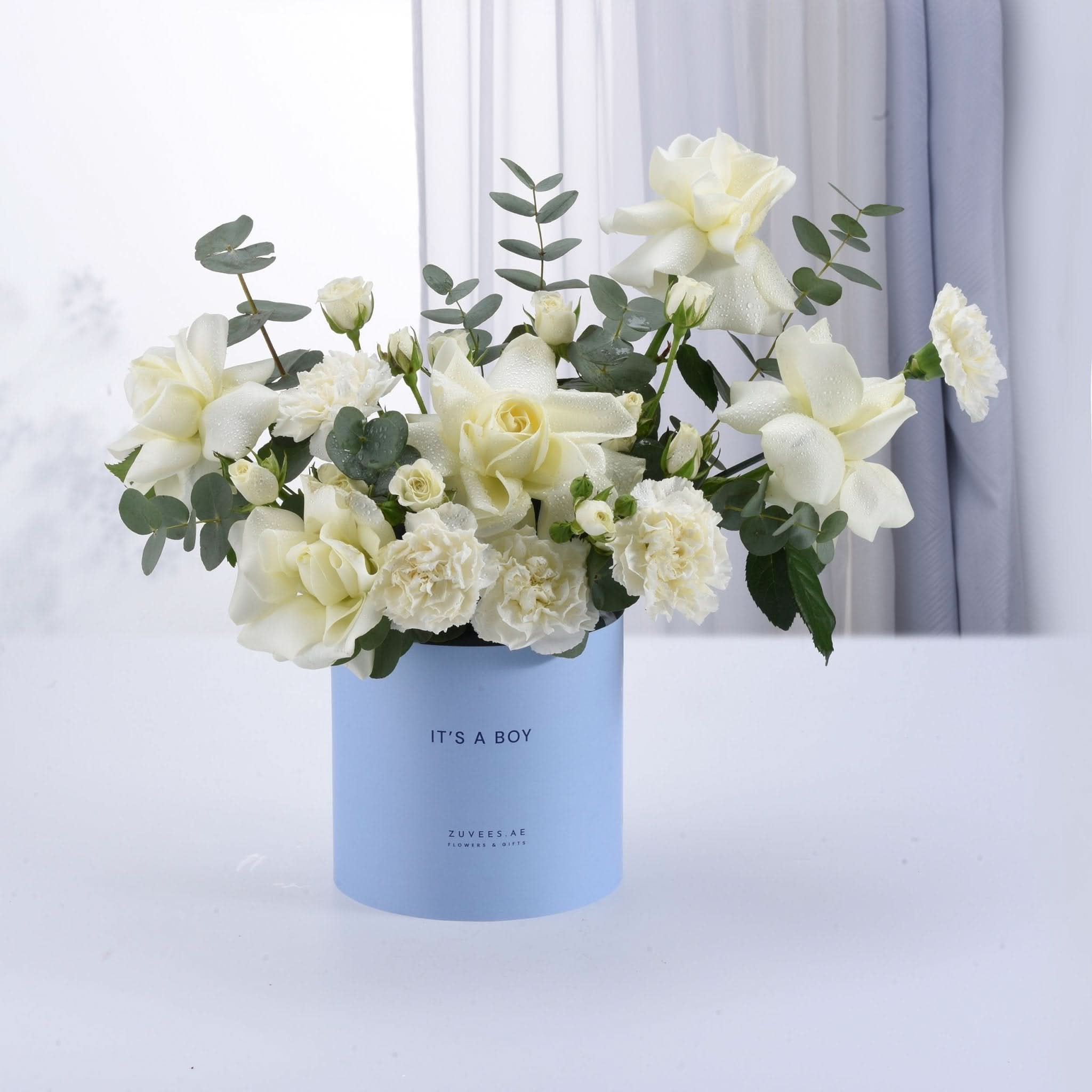 Light blue box holds dew-kissed white roses and eucalyptus, celebrating "It&