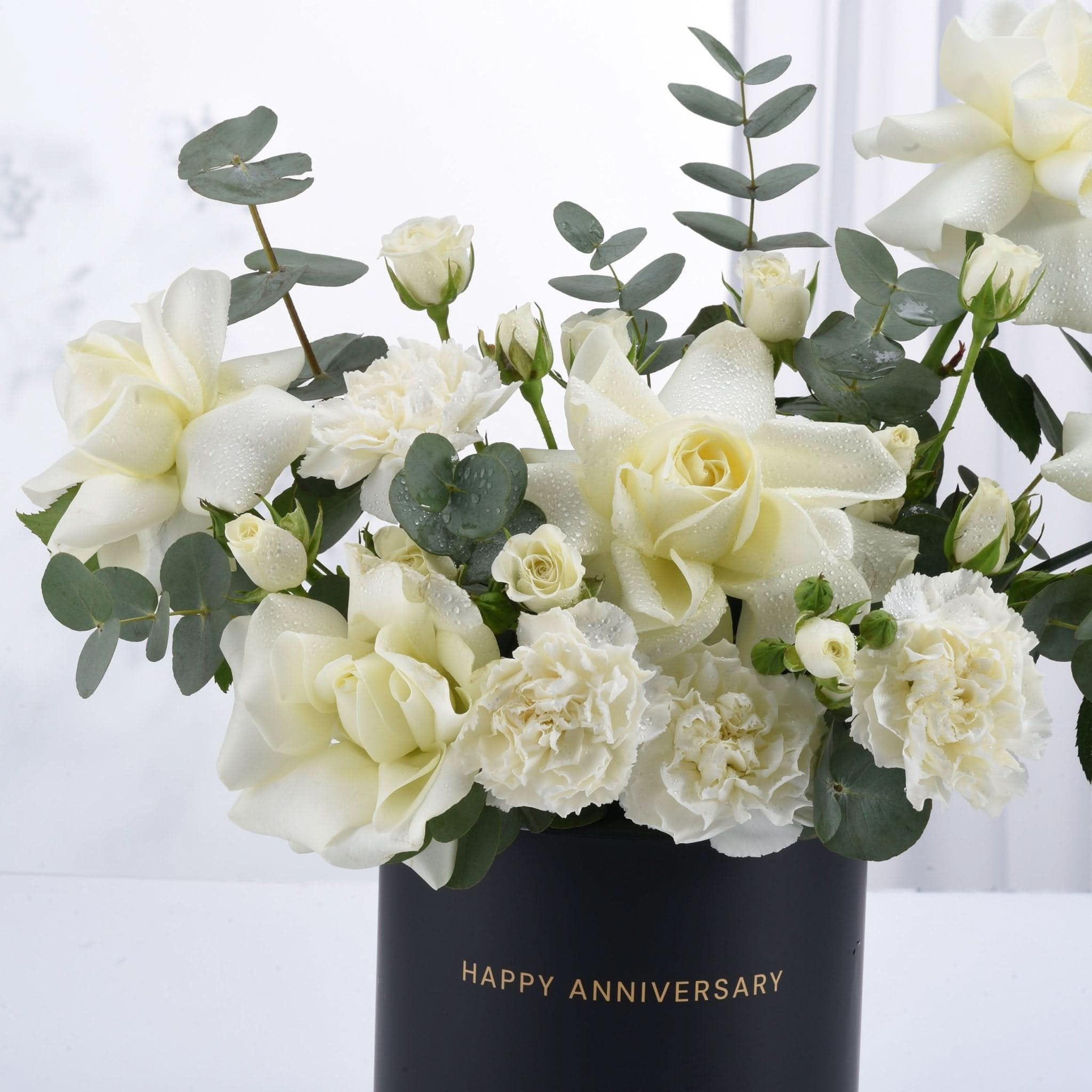 Elegant white roses and carnations with dewdrops in black "Happy Anniversary" vase.
