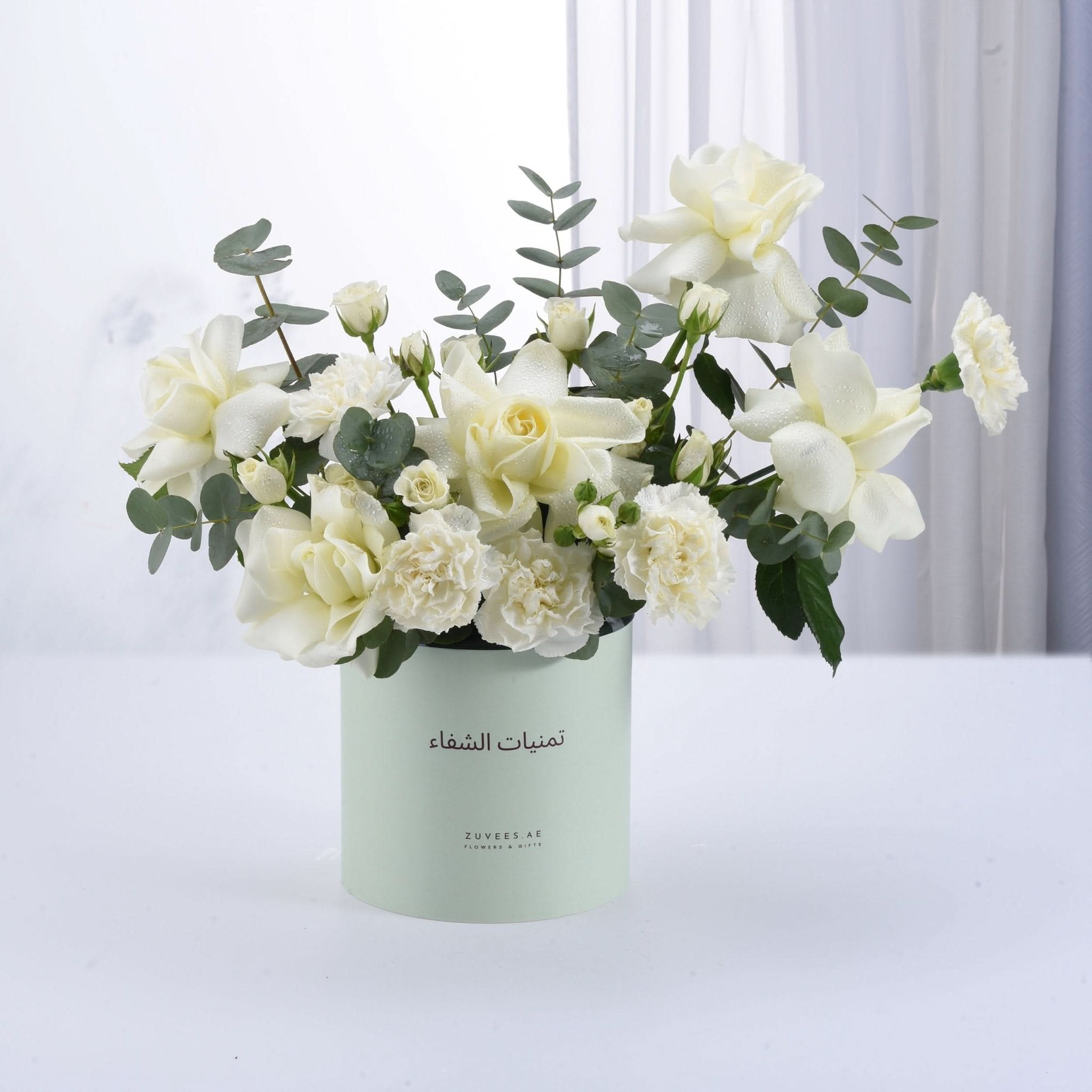 Elegant white rose and carnation bouquet in mint green cylindrical vase.