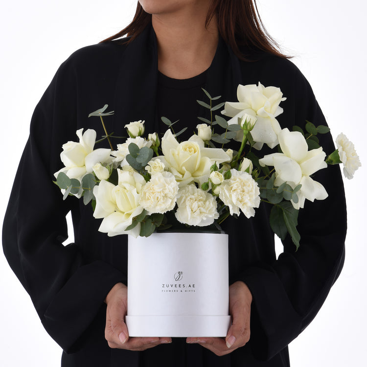 Elegant white roses and carnations in sleek white box, held by person in black.