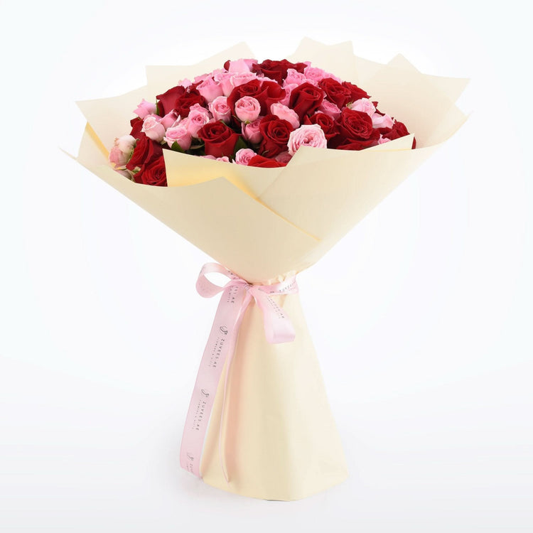 Vibrant red and pink roses wrapped in cream paper with pink ribbon bow.