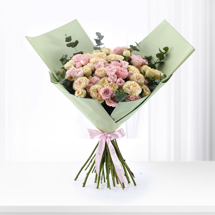 Pastel pink and cream roses wrapped in sage green paper with pink ribbon.
