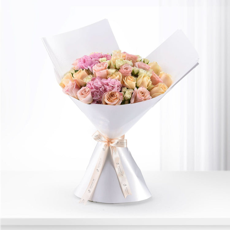 Soft pink and peach roses with hydrangeas, elegantly wrapped in white paper and ribbon.