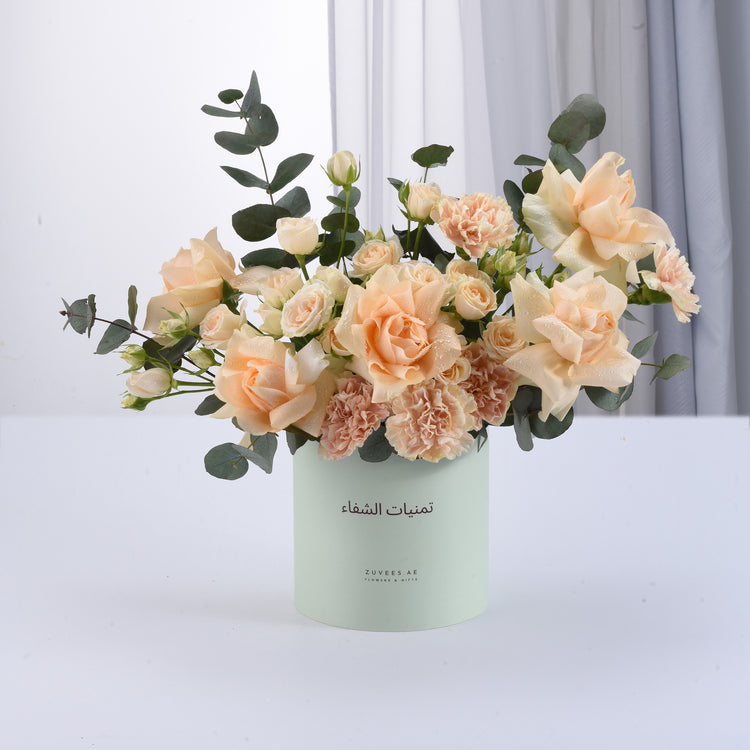 Pastel peach roses and carnations in mint container, dewy and elegant.
