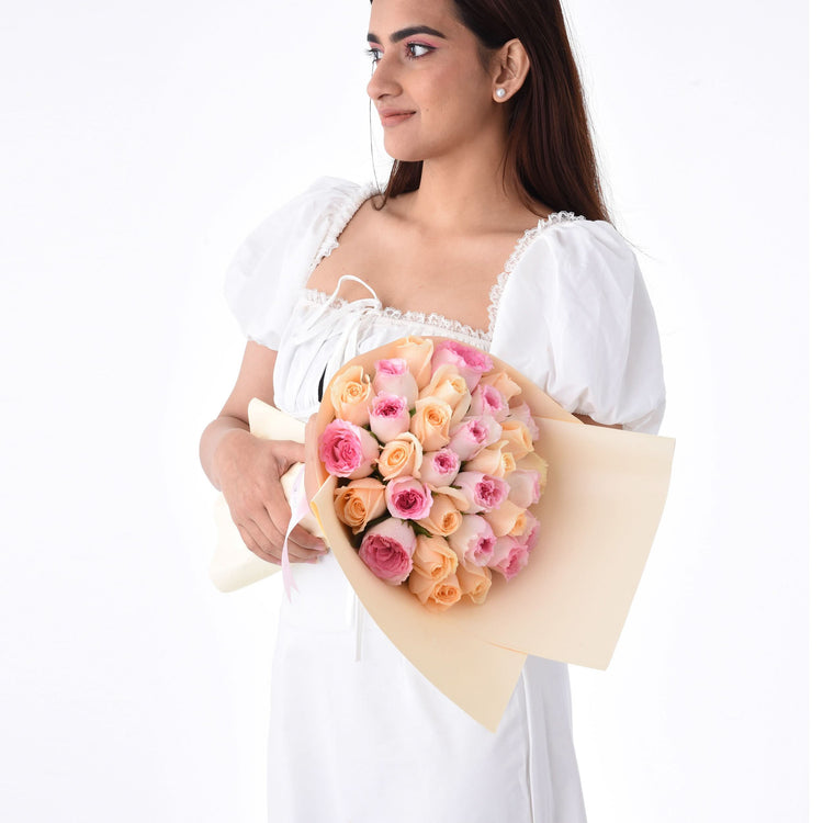 Woman in white dress holds pastel pink and peach rose bouquet.