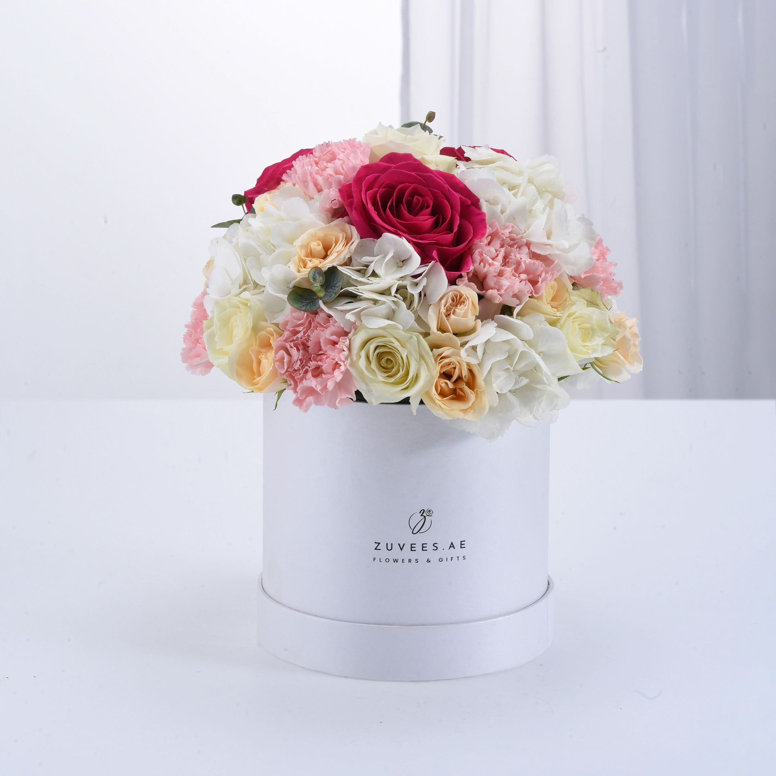 White box overflowing with vibrant pink, cream, and red roses, carnations, and hydrangeas.