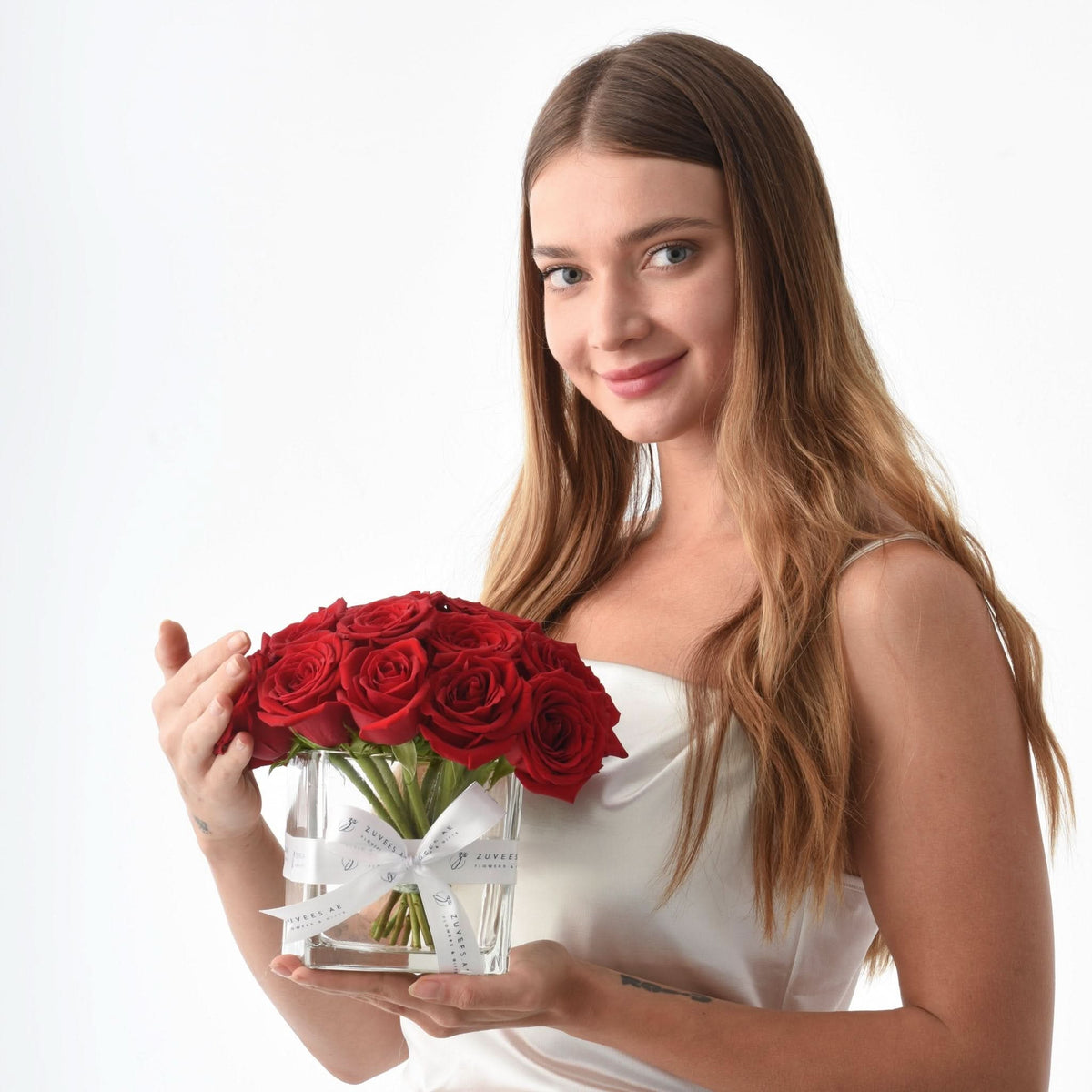 Woman holds vibrant red roses in clear glass vase with white ribbon.
