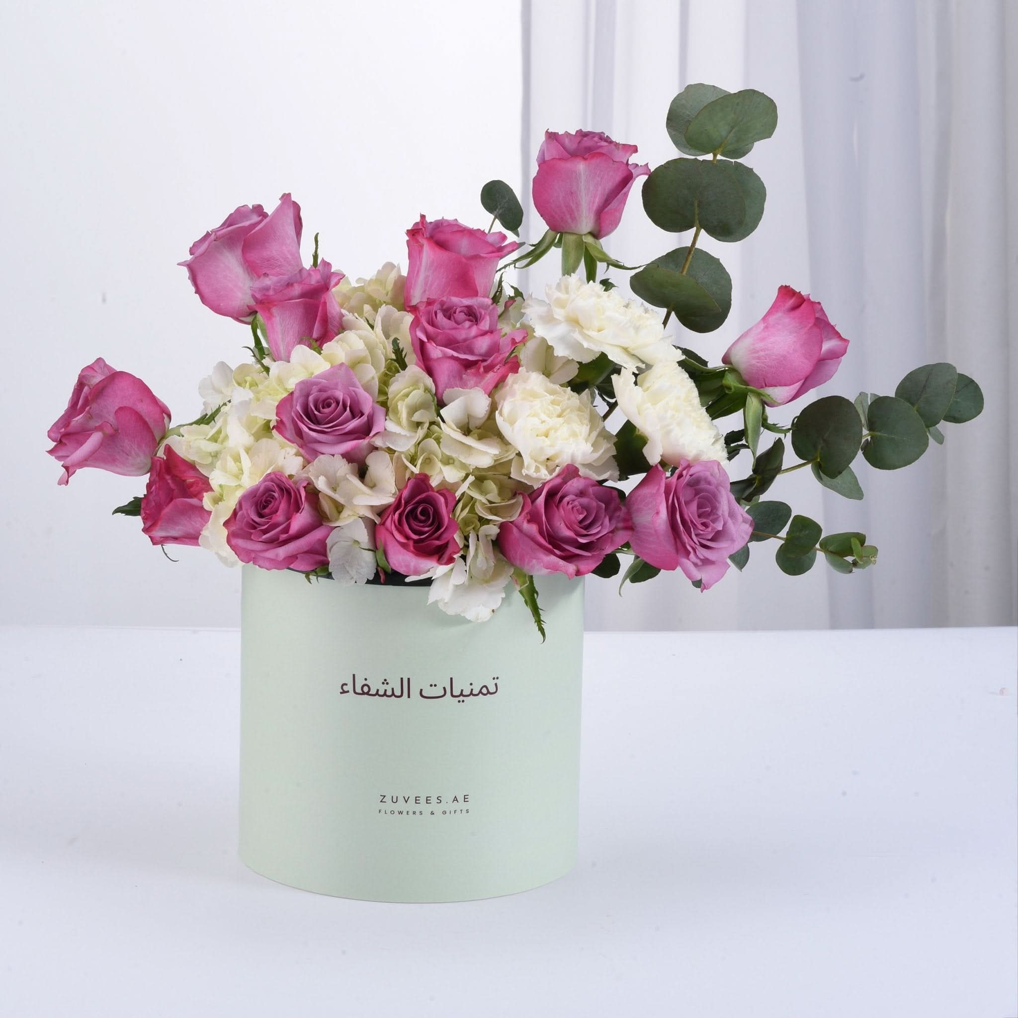 Pastel mint box holds vibrant pink roses, white hydrangeas, and eucalyptus.