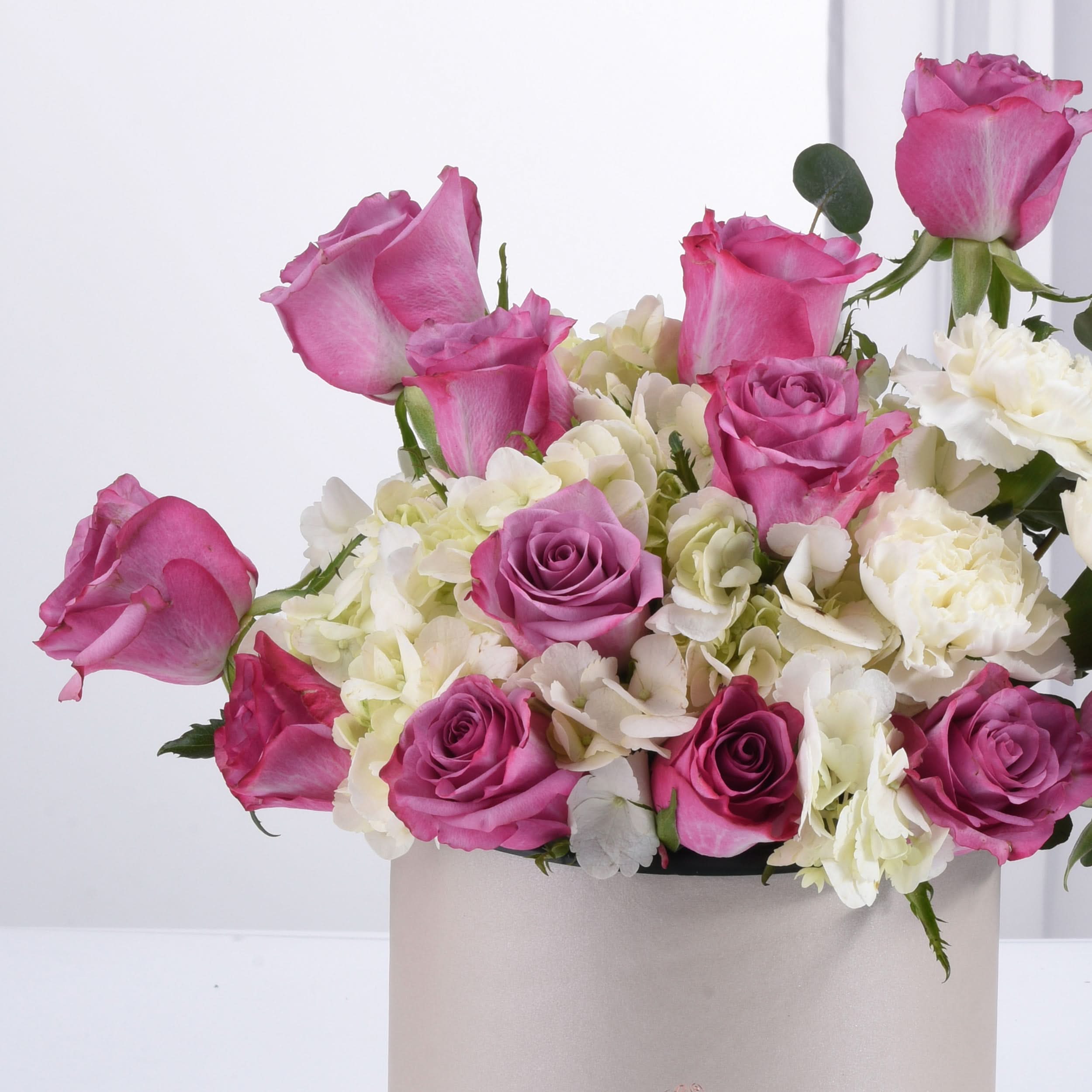 Pink roses, white hydrangeas, and carnations in a sleek silver box, elegant and fresh.