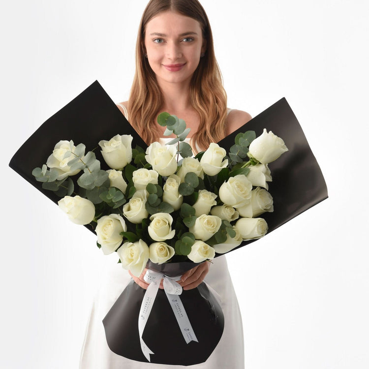 Elegant white roses wrapped in matte black paper with silver ribbon.