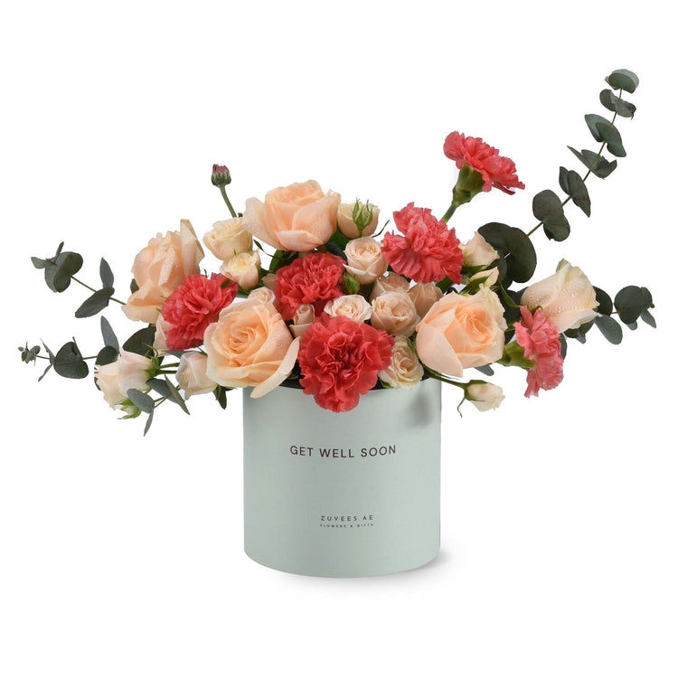 Pastel peach roses and coral carnations in mint box with "Get Well Soon" message.
