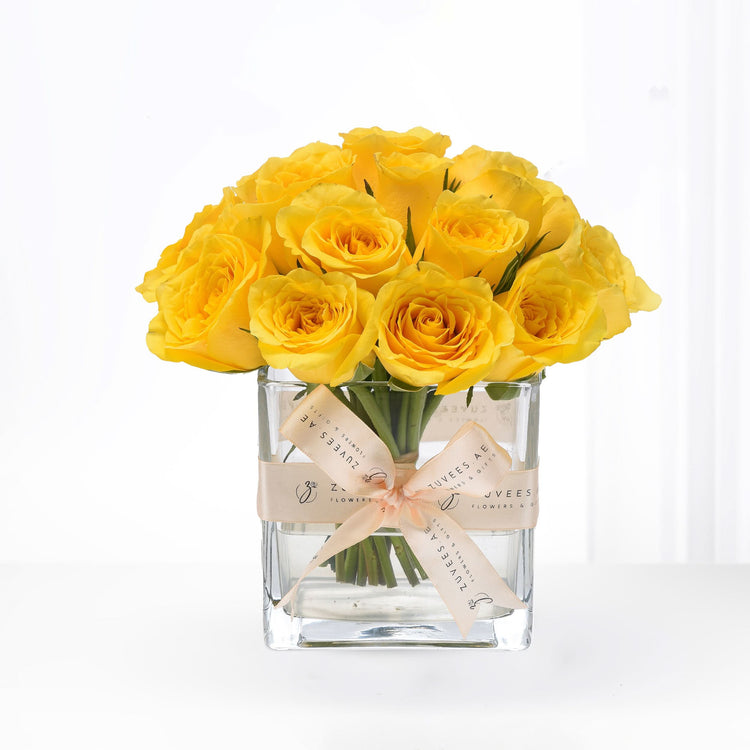 Vibrant yellow roses in clear glass vase, elegantly tied with branded beige ribbon.