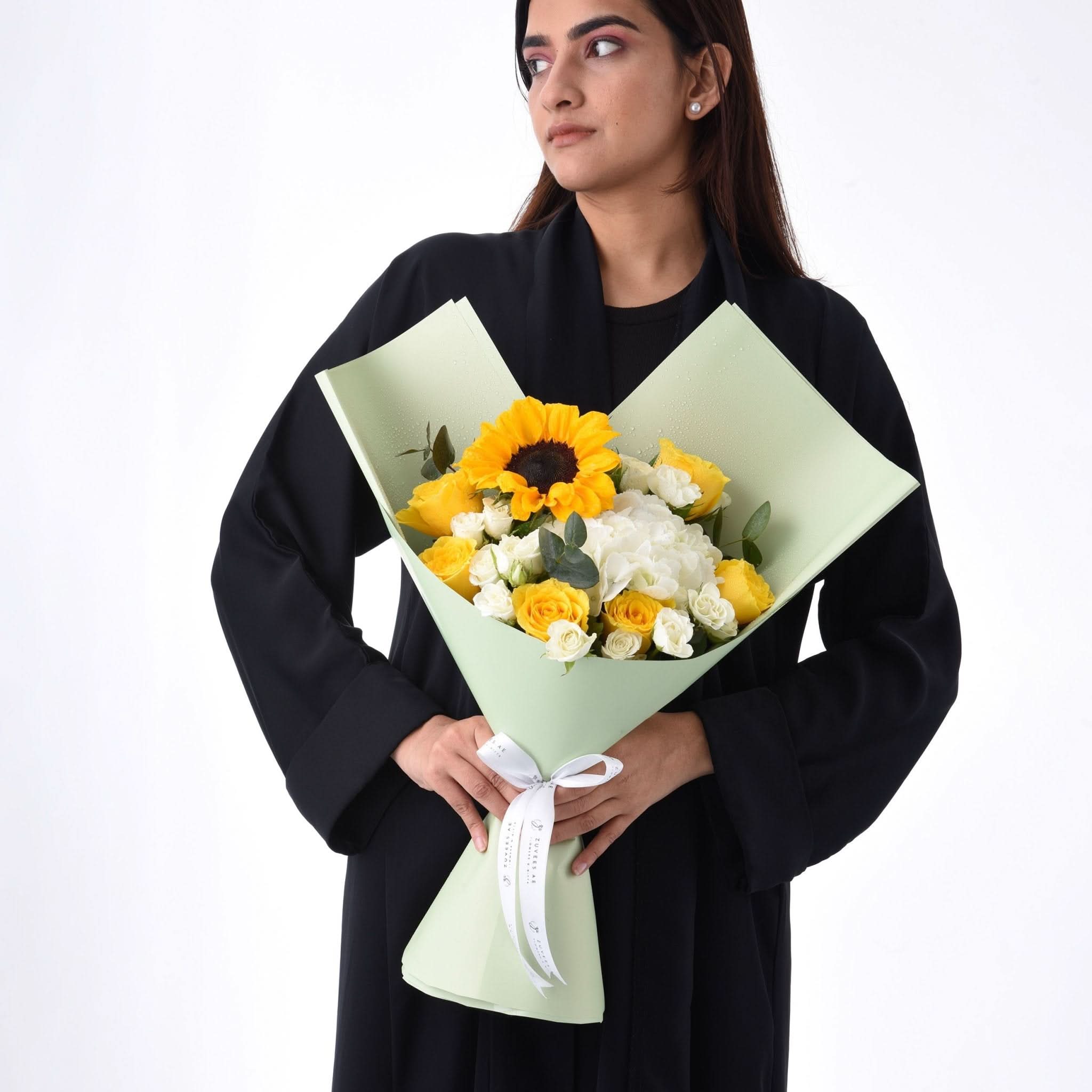 Woman holds vibrant yellow sunflower and rose bouquet in mint wrap.