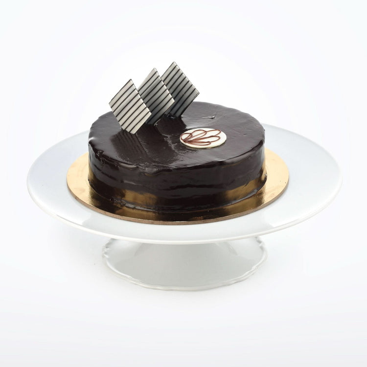 Glossy chocolate cake with striped shards, gold base, on white pedestal stand.