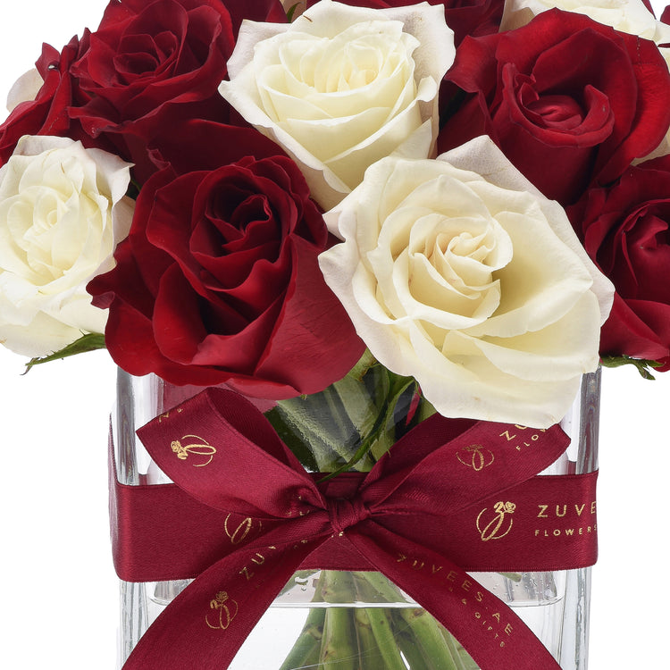 Luxurious red and white roses in clear vase, tied with burgundy ribbon featuring gold logo.