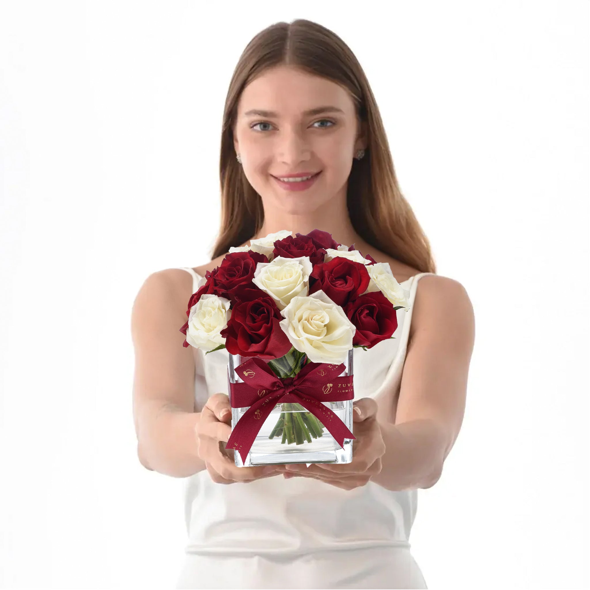 Woman holds elegant red and white rose bouquet in clear glass vase with burgundy bow.