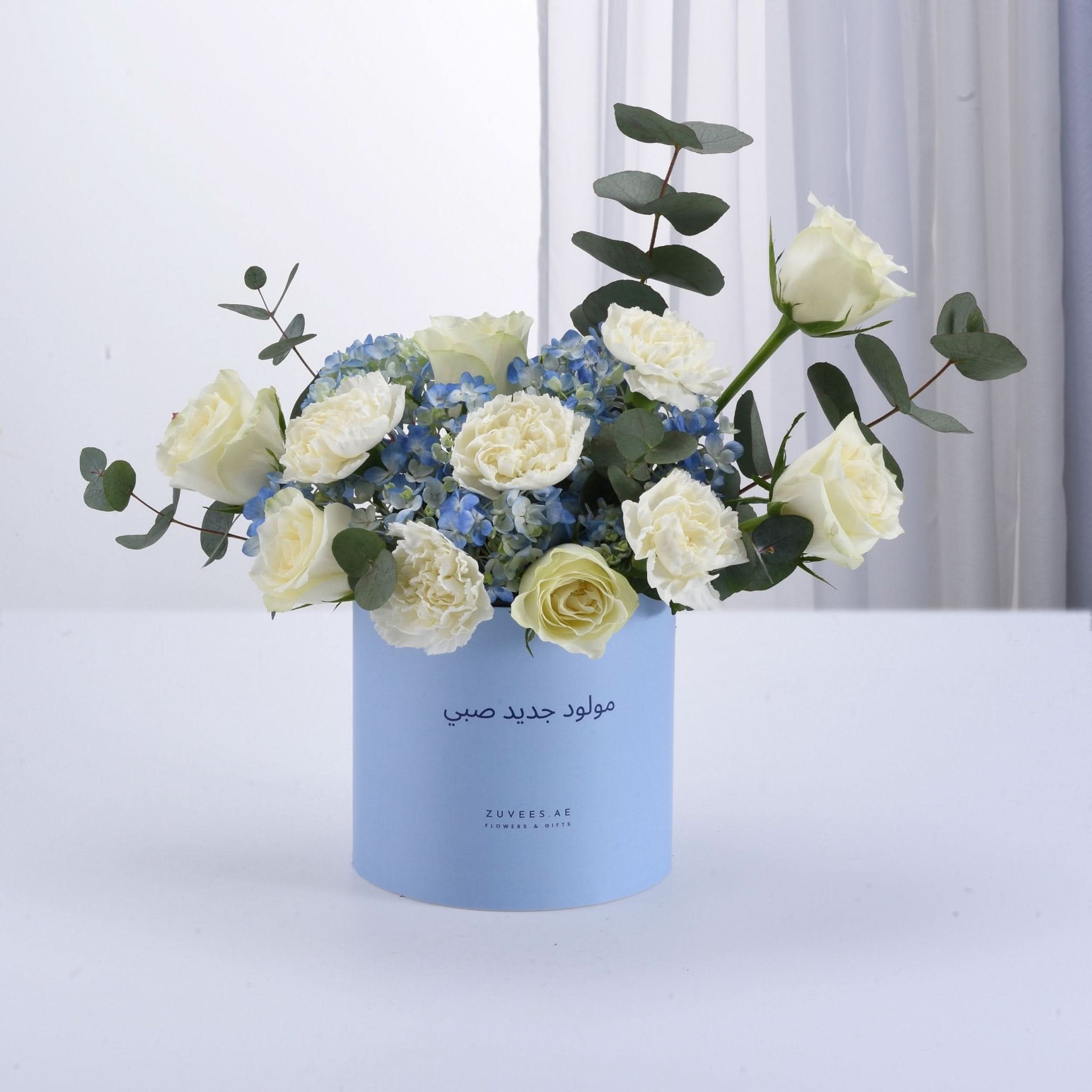 Light blue box holds white roses and blue hydrangeas with eucalyptus.