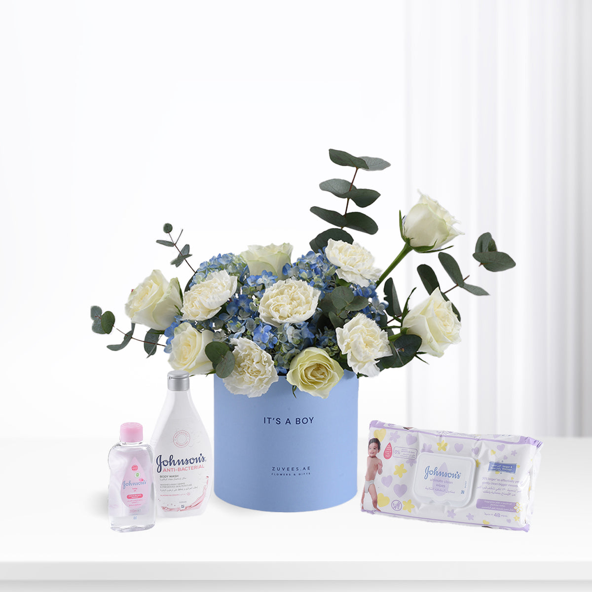 Soft blue floral arrangement with white roses and hydrangeas, paired with Johnson’s baby essentials for a boy.