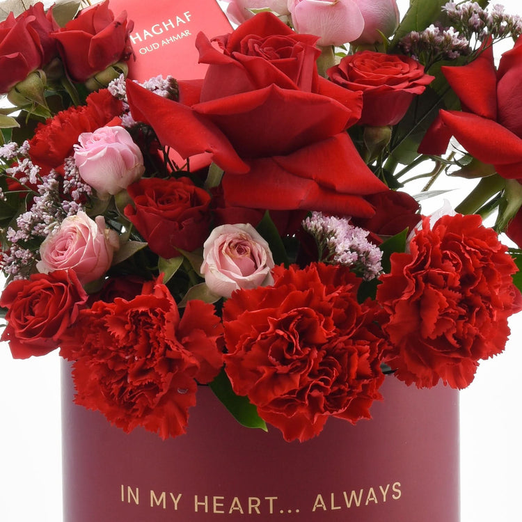 Vibrant red roses, carnations, pink blooms in deep red box with "IN MY HEART... ALWAYS" gold text.