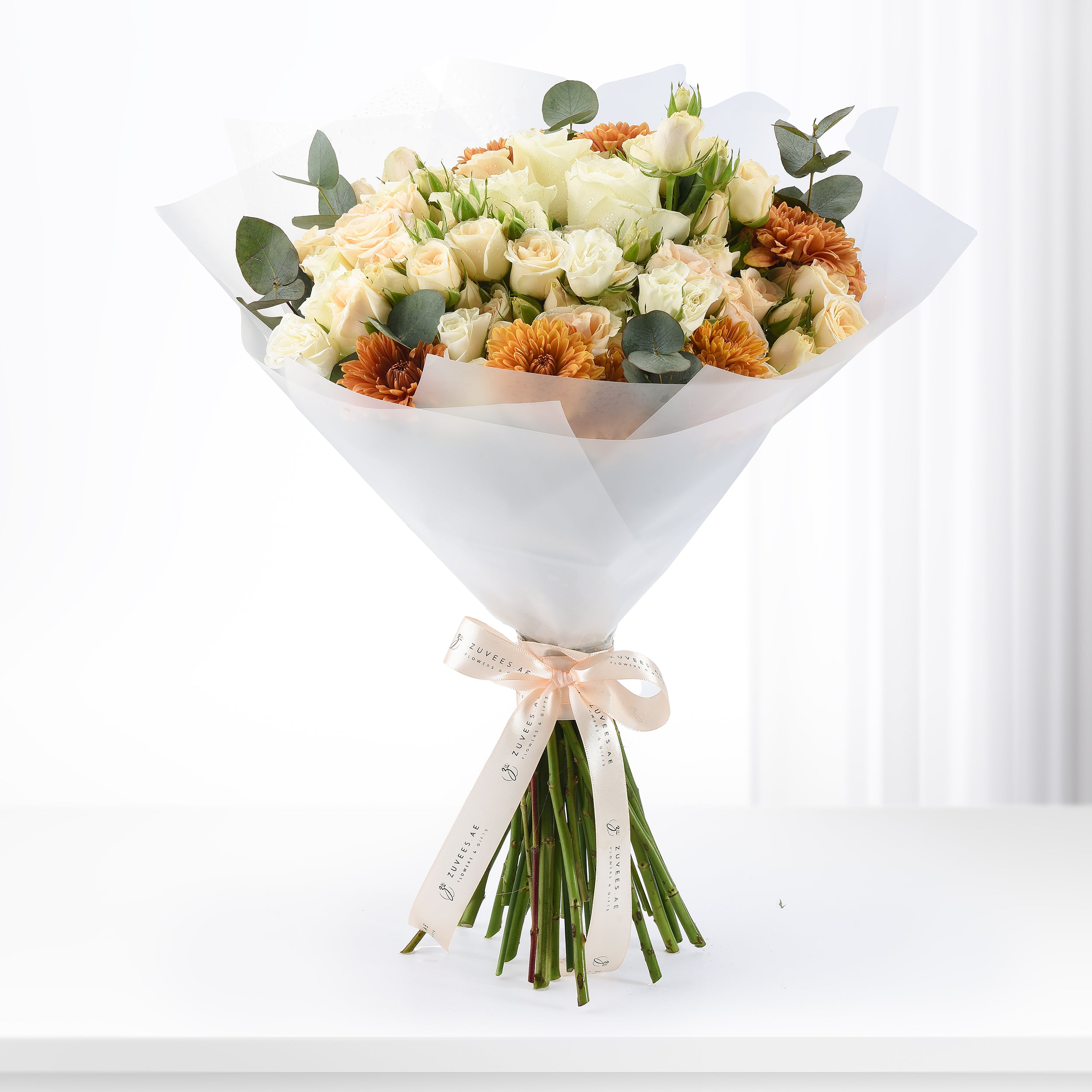 Cream roses and orange gerberas wrapped in white paper with branded ribbon.