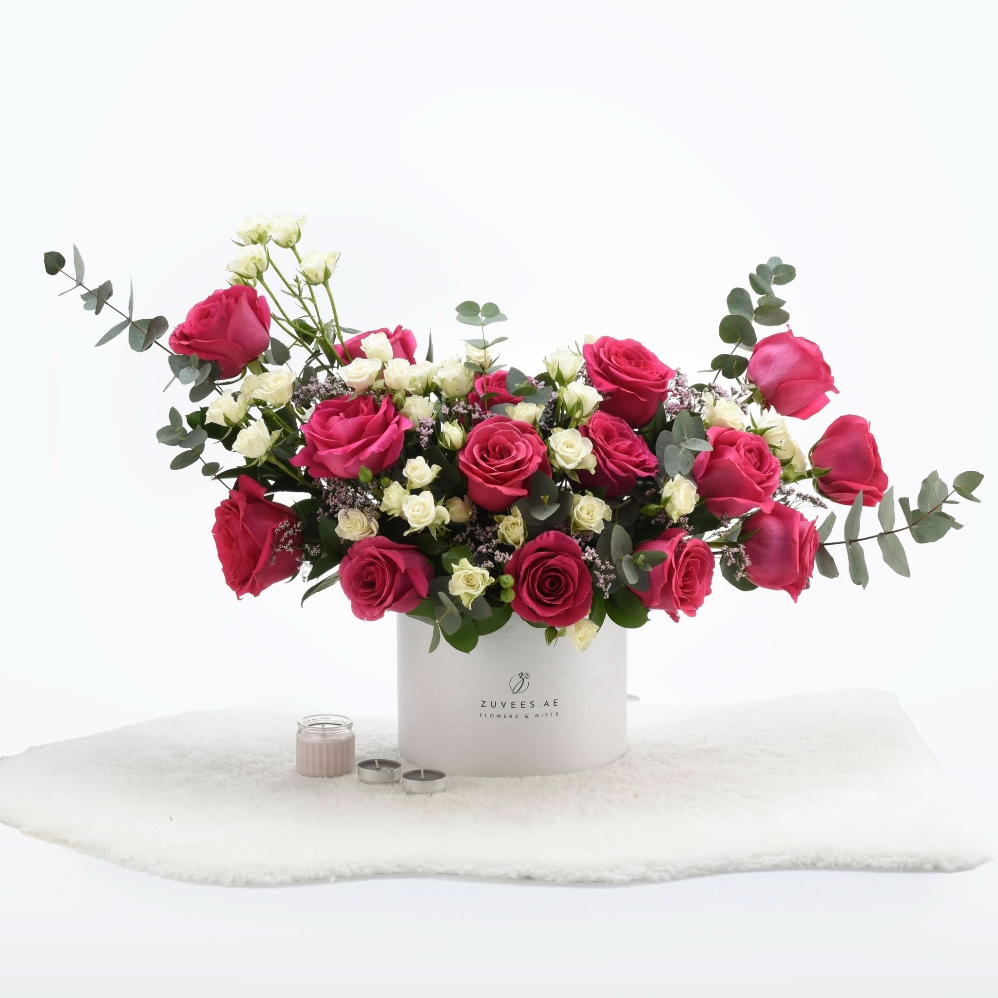 Vibrant pink and white roses in sleek white box, accented with eucalyptus and candles.