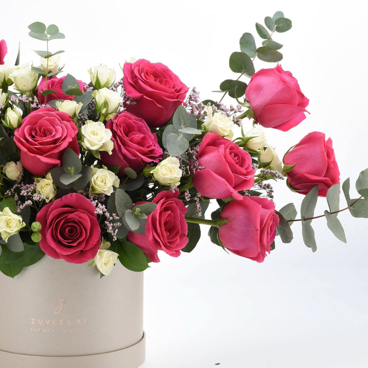 Vibrant pink and white roses cascade from beige box, accented with eucalyptus.