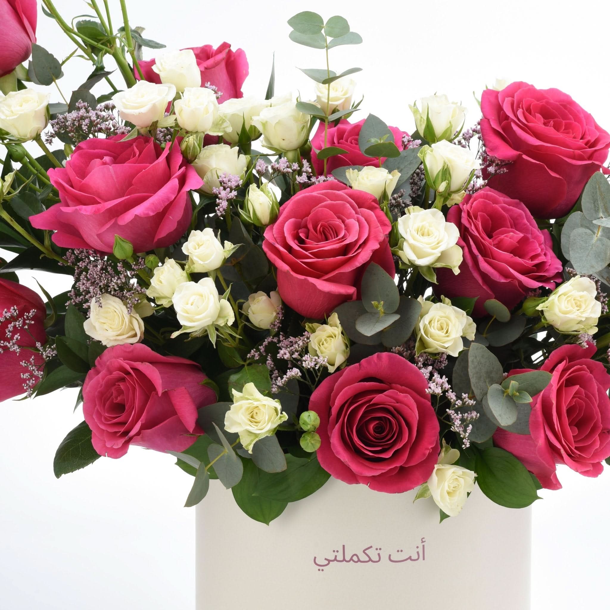 Vibrant pink and white roses with eucalyptus, Arabic message on vase.