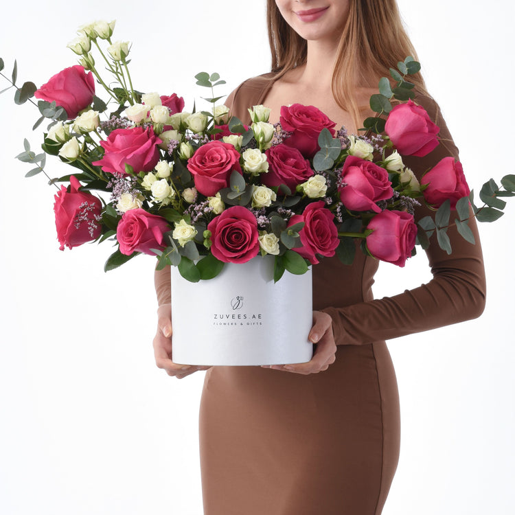Vibrant pink and white roses with eucalyptus in sleek white Zuvees box, held by woman in brown dress.