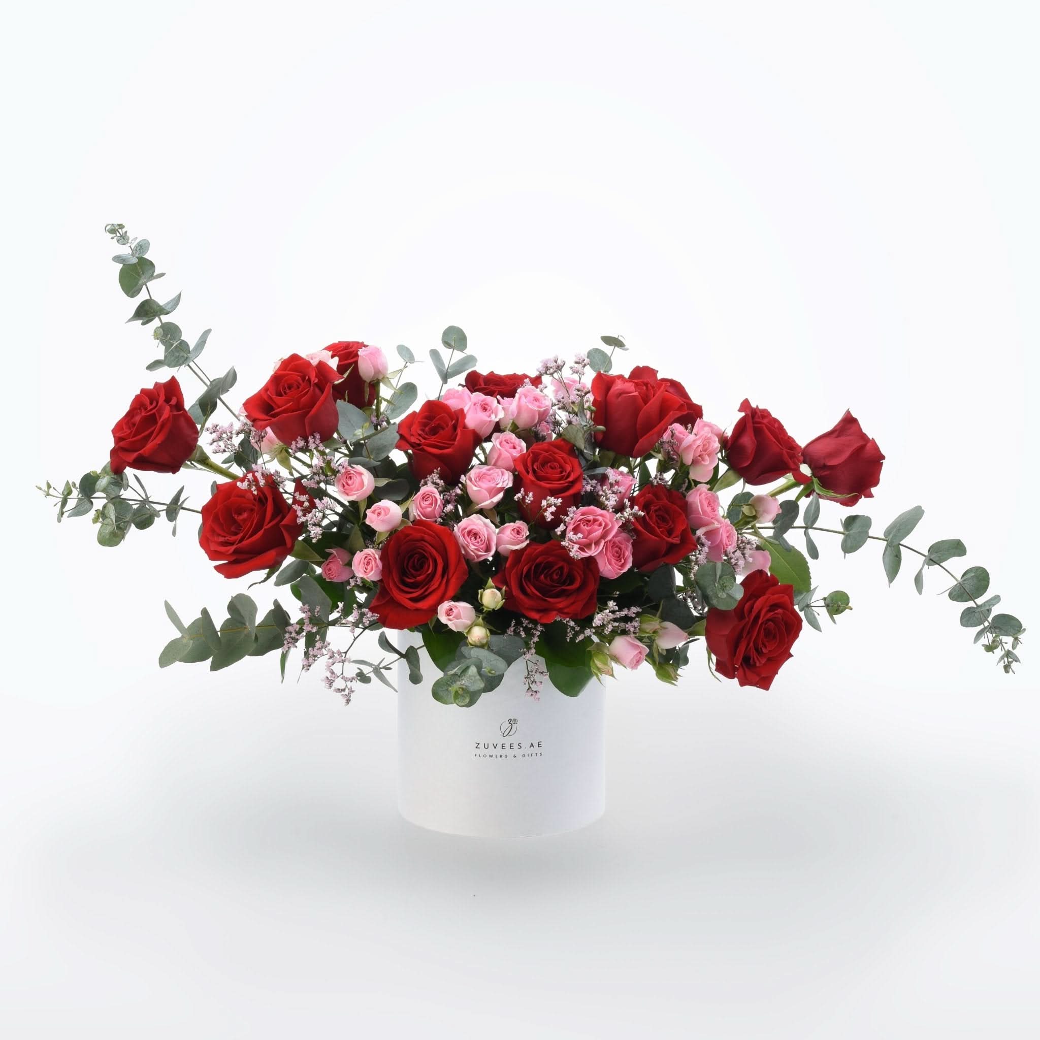 Vibrant red and pink roses with eucalyptus in sleek white Zuvees box, perfect gift.