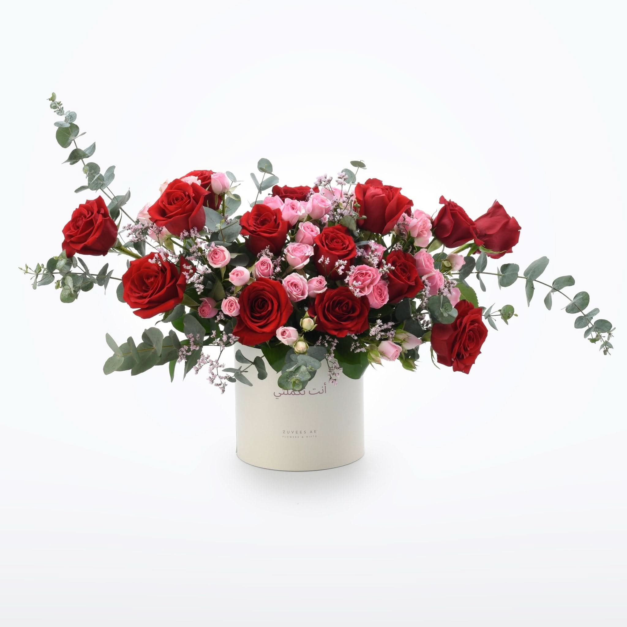 Vibrant red and pink roses in elegant white cylindrical vase with eucalyptus.